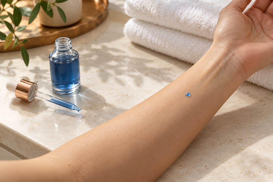 A small blue cosmetic serum drop on the inner forearm beside an unbranded bottle and dropper